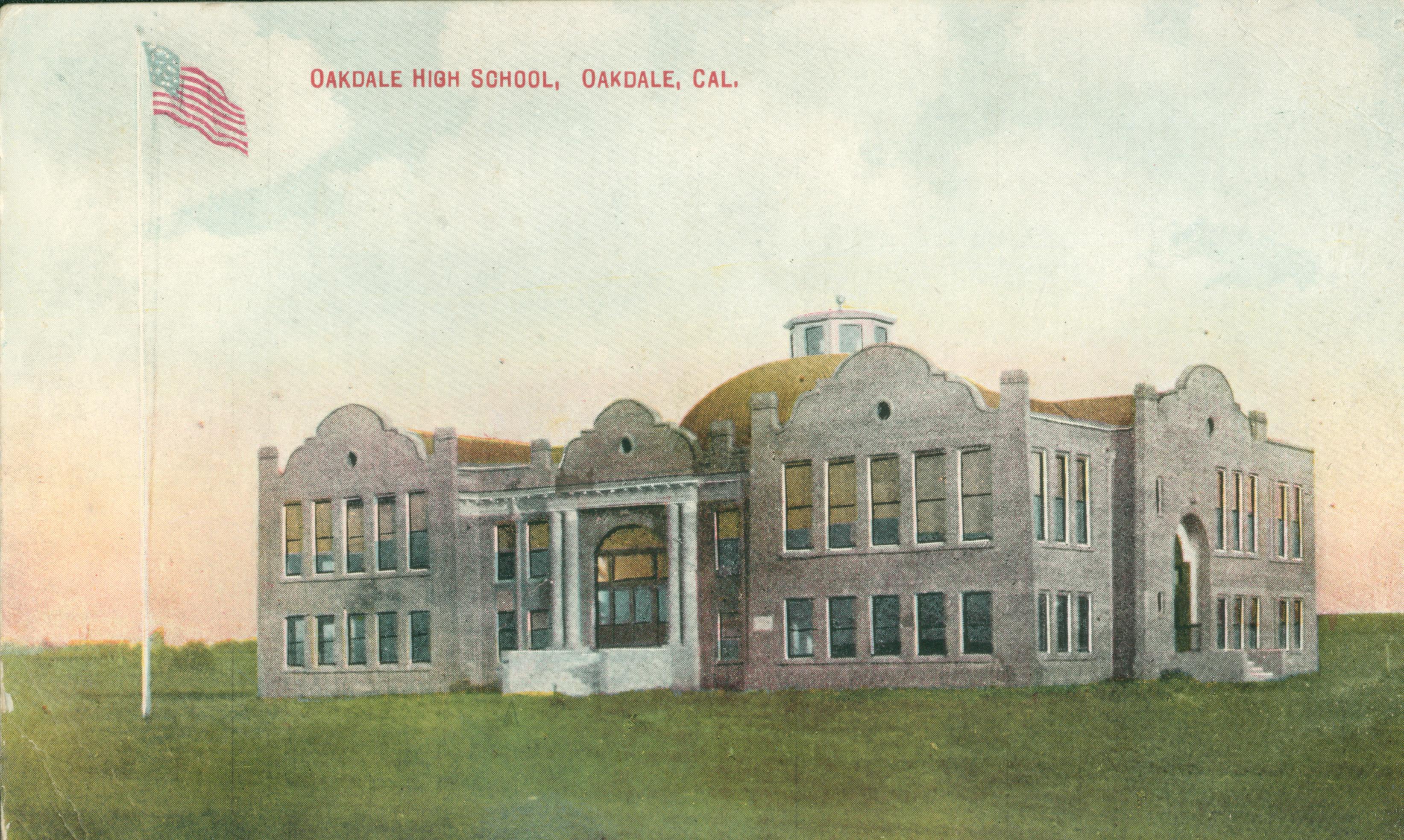 Shows a corner view of Oakdale High School in the middle of an open field with a flag pole out front